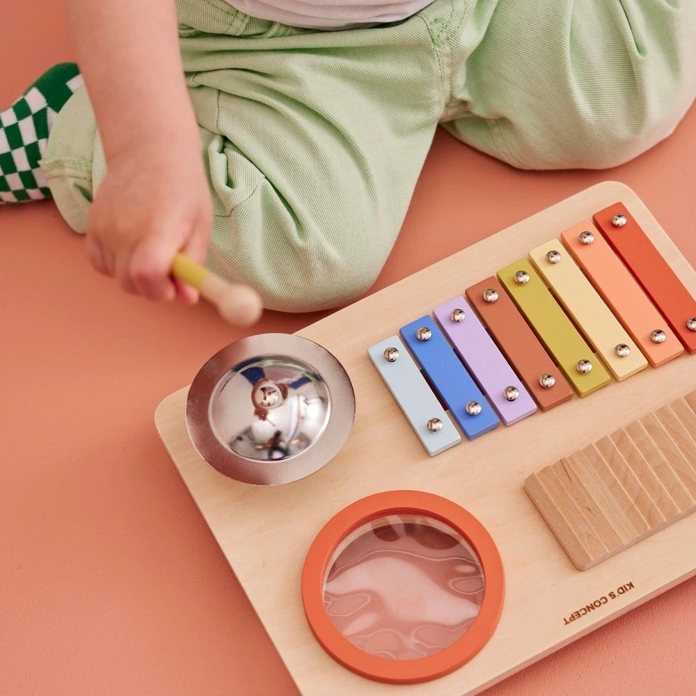 Drewniana tablica muzyczna Kid’s Concept dla dziecka od 3 lat – zestaw instrumentów 4w1 (bębenek, talerz, ksylofon, guiro) wspierający rozwój słuchu, poczucia rytmu i koordynacji u małego muzyka.