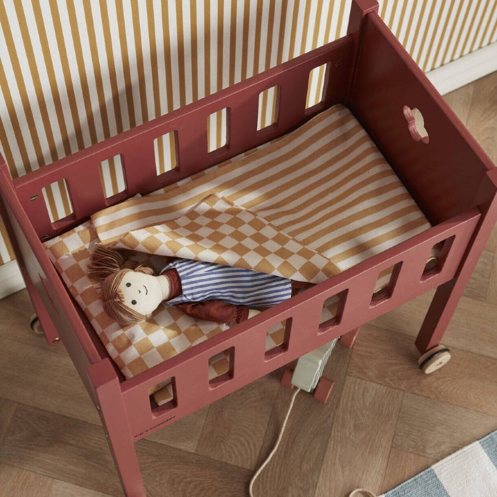 Drewniane łóżeczko dla lalek na kółkach Kid’s Concept dla dzieci od 3 lat – elegancka zabawka z bawełnianą pościelą w zestawie, rozwijająca empatię, opiekuńczość i umiejętności społeczne poprzez zabawę w odgrywanie ról.