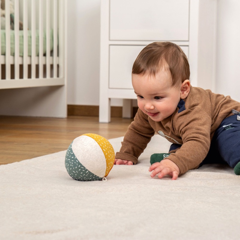 Lekka sensoryczna piłka z wbudowaną cichą grzechotką niemieckiej marki sigikid. Kolorowa pluszowa piłeczka dla niemowląt o średnicy 11 cm z materiałową pętelką do wózka, bezpieczna miękka zabawka rozwojowa od 3 miesięcy.